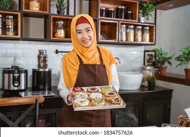 smiling hooded Asian woman wearing an apron carrying a packing box of donuts - Powered by Shutterstock