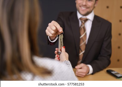 Smiling hotel manager handing over a door key to a woman customer after checking her in to the hotel, selective focus to his hand and the key