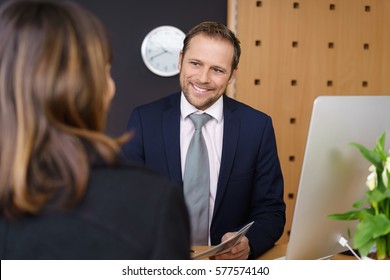 Smiling Hotel Manager Or Receptionist Attending To A Female Client In A Classy Hotel Standing With Her Bill Or A Brochure In His Hand
