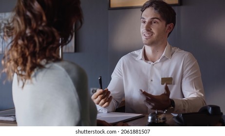 Smiling Hotel Receptionist Talking With Blurred Woman At Hotel Counter