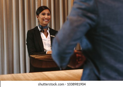 Smiling Hotel Receptionist Talking With Male Guest At Reception Counter. Happy Female Receptionist Worker Standing At Hotel Counter With Businessman Checking In.