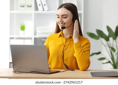 Smiling hotline operator in headset having videocall with client by laptop at table in office