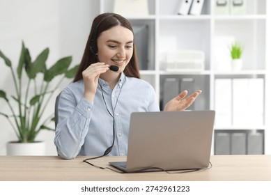 Smiling hotline operator in headset having videocall with client by laptop at table in office