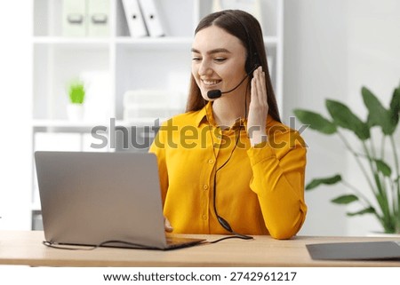 Smiling hotline operator in headset having videocall with client by laptop at table in office