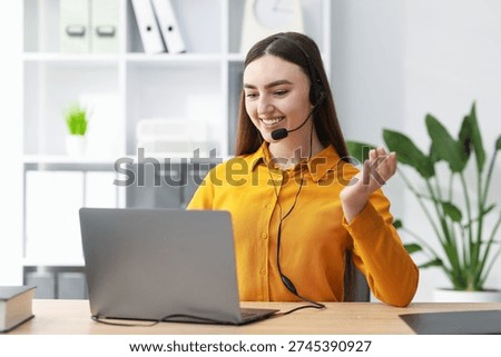 Smiling hotline operator in headset having videocall with client by laptop at table in office