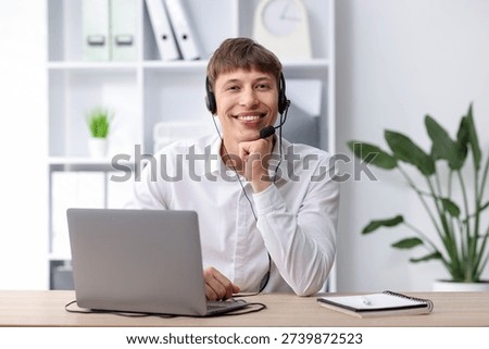 Smiling hotline operator in headset working with laptop at table in office