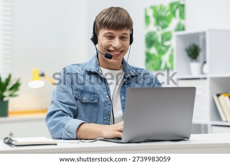 Smiling hotline operator in headset working with laptop at table in office