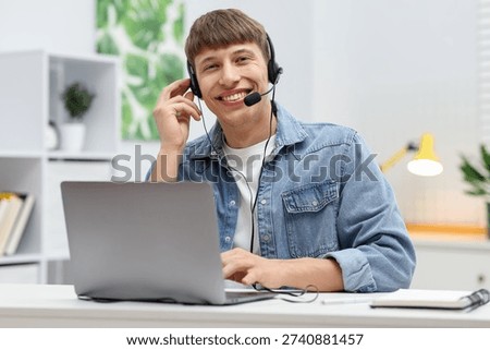 Smiling hotline operator in headset working with laptop at table in office