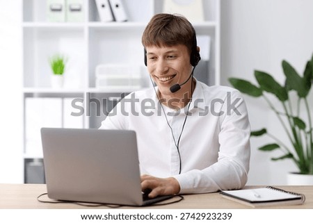Smiling hotline operator in headset working with laptop at table in office