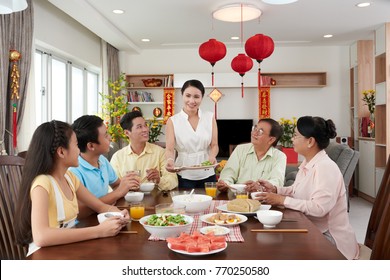 Smiling housewife bringing main dish to the Tet dinner; couplets with best wishes for the upcoming year in the background