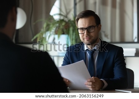 Smiling hr manager sit at desk opposite male candidate on vacant post study cv hold job interview. Young man recruiter in formal attire glasses ask applicant questions about professional experience Foto stock © 