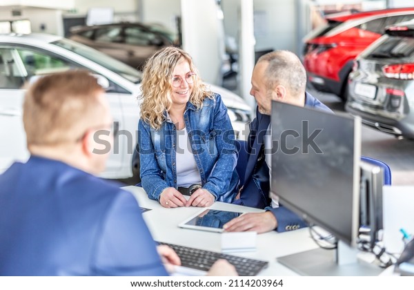 Smiling\
husband and wife look at each other deciding which car they want\
sitting across the table with sales\
manager.
