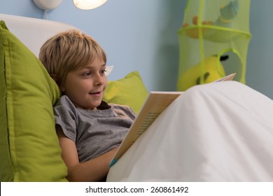 Smiling ill boy reading book in bed - Powered by Shutterstock