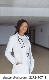 Smiling Image Of Nigerian Young Medical Student Weeing White Coat Uniform And Stethoscope Posing At Sunny Day In Clinic Hall.  Healthcare System And Medical Education In Africa.