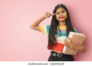 Smiling Indian Asian girl posing isolated holding notebooks and winking eyes with her hands on head thinking or imagining about an interesting idea which will lead to success with mockup copy space