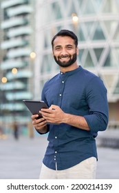 Smiling indian business man professional executive manager holding digital tablet online fintech outside, happy eastern businessman ceo using pad standing outdoors in big urban city street, vertical. - Shutterstock ID 2200214139