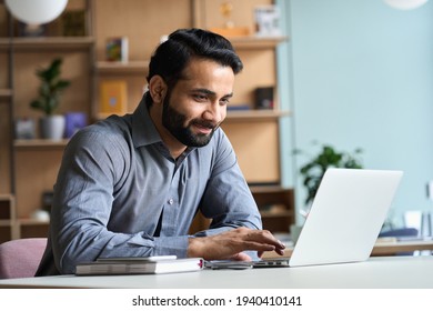 Smiling indian business man working on laptop at home office. Young indian student or remote teacher using computer remote studying, virtual training, watching online education webinar at home office. - Shutterstock ID 1940410141