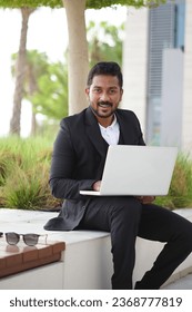 Smiling indian business man working on laptop at park. Young indian student or remote teacher using computer remote studying, virtual training, watching online education webinar - Shutterstock ID 2368777819
