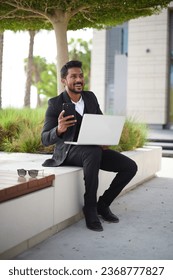 Smiling indian business man working on laptop at park. Young indian student or remote teacher using computer remote studying, virtual training, watching online education webinar - Shutterstock ID 2368777827
