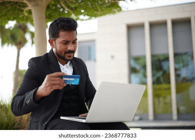 Smiling indian business man working on laptop at park. Young indian student or remote teacher using computer remote studying, virtual training, watching online education webinar - Shutterstock ID 2368777833