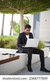 Smiling indian business man working on laptop at park. Young indian student or remote teacher using computer remote studying, virtual training, watching online education webinar - Shutterstock ID 2368777839