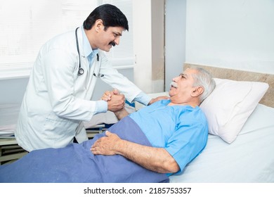 Smiling Indian caring doctor supporting putting hand on shoulder of olde senior male patient lying on bed at clinic or hospital. Elderly people health care concept. - Shutterstock ID 2185753357
