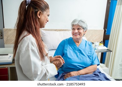 Smiling Indian Caring Doctor Supporting Holding Hand Of Olde Senior Female Patient Lying On Bed At Clinic Or Hospital. Elderly People Health Care Concept.