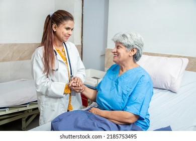 Smiling Indian Caring Doctor Supporting Holding Hand Of Olde Senior Female Patient Lying On Bed At Clinic Or Hospital. Elderly People Health Care Concept.