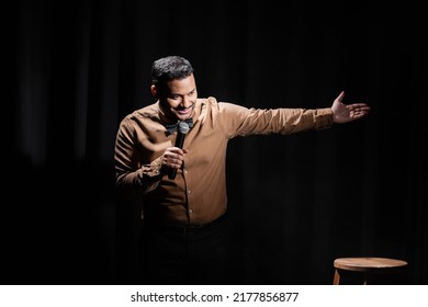 Smiling Indian Comedian Performing Stand Up Comedy Into Microphone On Black