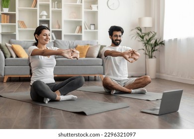 Smiling Indian Couple Stretching Up Together In Front Of Laptop, Happy Eastern Spouses Doing Home Workout, Making Domestic Fitness Training, Exercising On Fitness Mat In Living Room, Free Space - Powered by Shutterstock