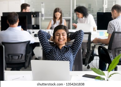 Smiling Indian Female Employee Relaxing Leaning Back In Chair With Hands Over Head At Workplace, Looking At Laptop Screen, Received Good News, Results, Business Achievement, Feeling Satisfied