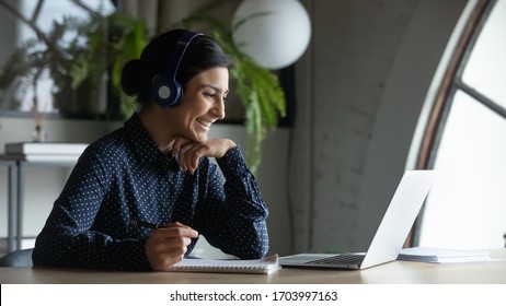 Smiling Indian female employee in wireless earphones talk on video call, have web conference with colleagues, happy ethnic woman worker in headset watch webinar on modern laptop at home - Shutterstock ID 1703997163