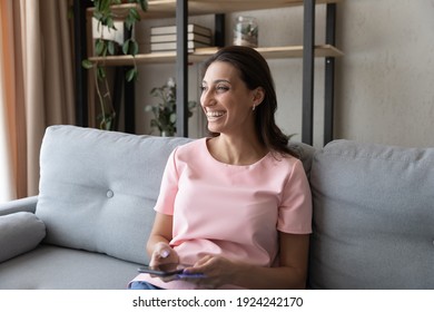 Smiling indian female hold credit card smartphone prepare to make provide electronic payment. Young arabic woman sit on sofa prepay ordered goods at web shop satisfied with easy convenient banking app