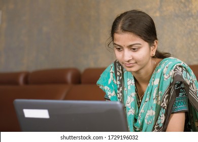 Smiling Indian Girl Student Or Employee Busy On Laptop Sit At Home In Casual Dress, Happy Woman Studying, E-learning, Using Online Software Or Technology App For Work, Education Concept.