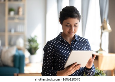 Smiling Indian Girl Student Professional Holding Using Digital Tablet Computer Online App Stand At Home Office, Young Ethnic Woman Surfing Internet Social Media Read Electronic Book In Modern Ereader