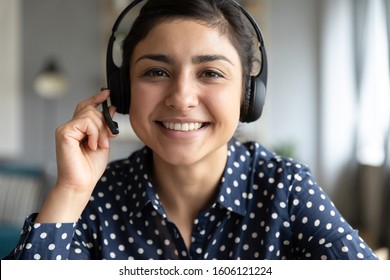 Smiling indian girl teacher counselor telesales agent wear wireless headset look at camera webcam, distance teaching, customer support service concept, telemarketing professional closeup portrait