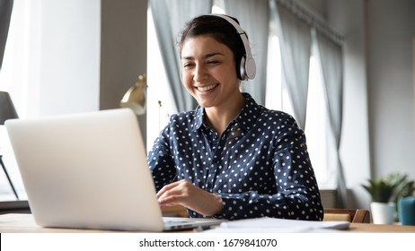Smiling Indian girl wearing headphones using laptop, looking at screen, happy young female listening to favorite music while working online on project, excited student learning language - Shutterstock ID 1679841070