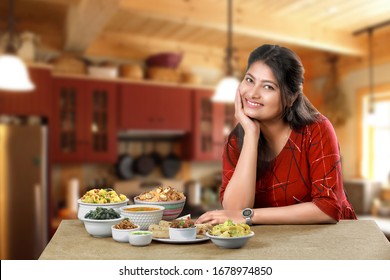 Smiling Indian Girl Or Woman Sitting In Relax Mood Beside Group Of Traditional Indian Dishes And Looking At The Camera. Female Model Potrait