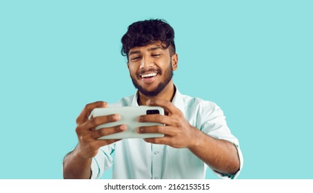 Smiling Indian Guy Isolated On Blue Studio Background Talk On Video Call On Cellphone Gadget. Happy Biracial Young Man Have Webcam Event On Smartphone. Online Communication Concept.