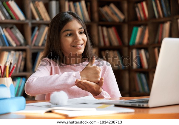 Smiling indian latin deaf disabled child school\
girl learning online class on laptop communicating with teacher by\
video conference call using sign language showing hand gesture\
during virtual lesson.