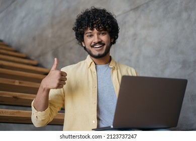 Smiling Indian man freelancer using laptop computer showing thumb up  looking at camera working online from home.  Asian student studying, watching training courses, online education concept 