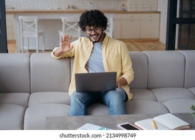 Smiling Indian Man Having Video Call Waving Hand Talking To Camera. Handsome Young Freelancer Communication Online Working From Home. Webinar, Video Conferencing, Online Meeting Concept