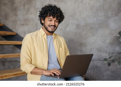 Smiling Indian man using laptop computer typing working freelance project from home. Handsome asian student studying, learning language, online education concept. Programmer sitting at workplace  - Shutterstock ID 2126525276