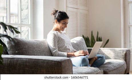 Smiling Indian Millennial Girl Sit Relax On Couch Using Modern Laptop Browsing Unlimited Wireless Internet, Happy Young Woman Freelancer Work On Computer Typing Texting From Home, Technology Concept