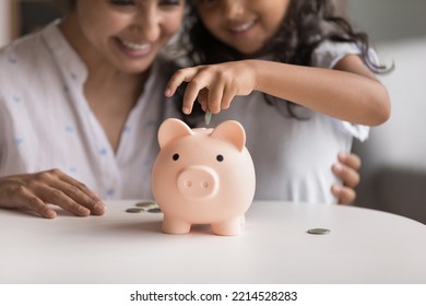 Smiling Indian Mom And Her Little 6s Cute Daughter Dropping Coins Into Piggy Bank. Loving Parent Teach Child Be Thrifty, To Save Pocket Money For Future Education Or Purchases, Think About Tomorrow