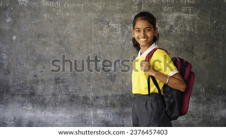 Smiling Indian Rural school girl with backpack looking at camera. Cheerful kid wearing school uniform with a big smile. Elementary and primary school education.