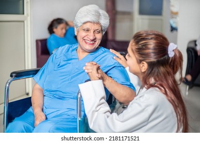 Smiling Indian Senior Lady Patient Looking At Female Doctor In Hospital Ward While Sitting On Wheel Chair, Holding Hand In Support, Old People Healthcare Concept.