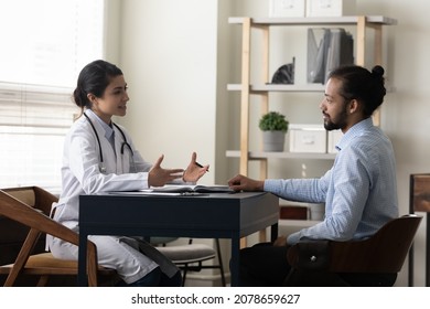 Smiling Indian Woman Doctor Talking, Consulting African American Man Patient At Meeting In Hospital, Young Female Physician Practitioner Giving Recommendation, Discussing Checkup Or Symptoms