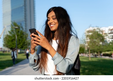 Smiling Indian Woman Holding Mobile Phone Shopping Online On The Street. Happy Asian Tourist Using Mobile App Searching Way. Travel Concept