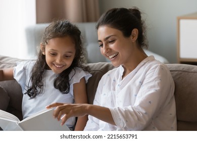 Smiling Indian woman read a book to little daughter, preschooler 6s adorable girl sits on sofa enjoy mothers storytelling spend leisure together at home. Children development, hobby, good life habit
